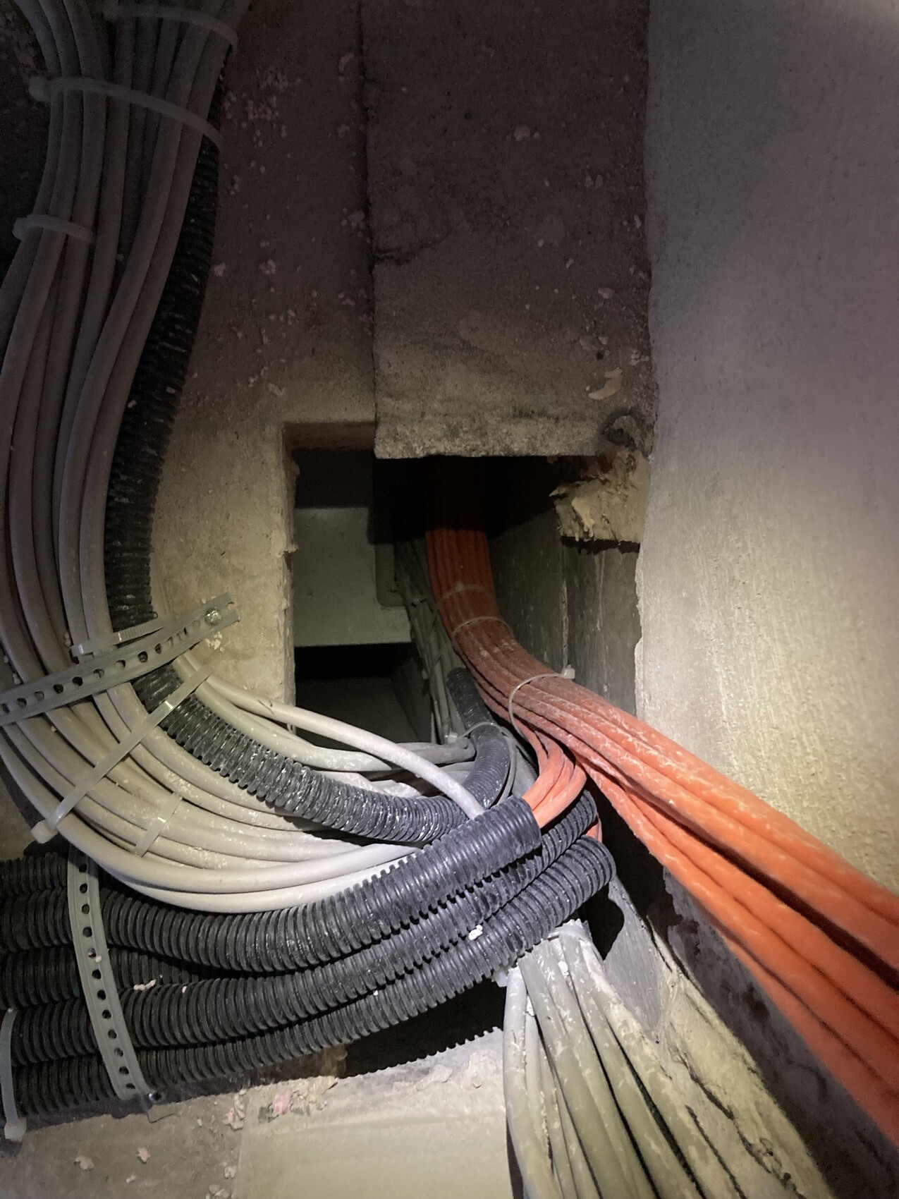 Kabelbündel in einer Wandöffnung: orange Kabel, graue/weiße Leitungen mit Schutzrohren.