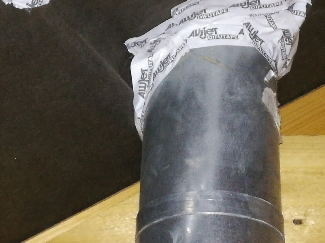 Dunkles Metallrohr steht senkrecht auf einer Holzplatte; Oberkante mit weißem Klebeband umwickelt.