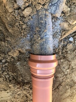 Nahaufnahme eines orangefarbenen PVC-Rohrs im Boden bei Bauarbeiten