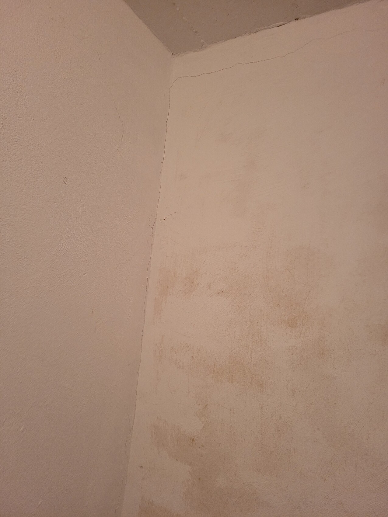 Zimmerecke mit verputzter Wand, sichtbare Risse und ungleichmäßige beige Flecken.