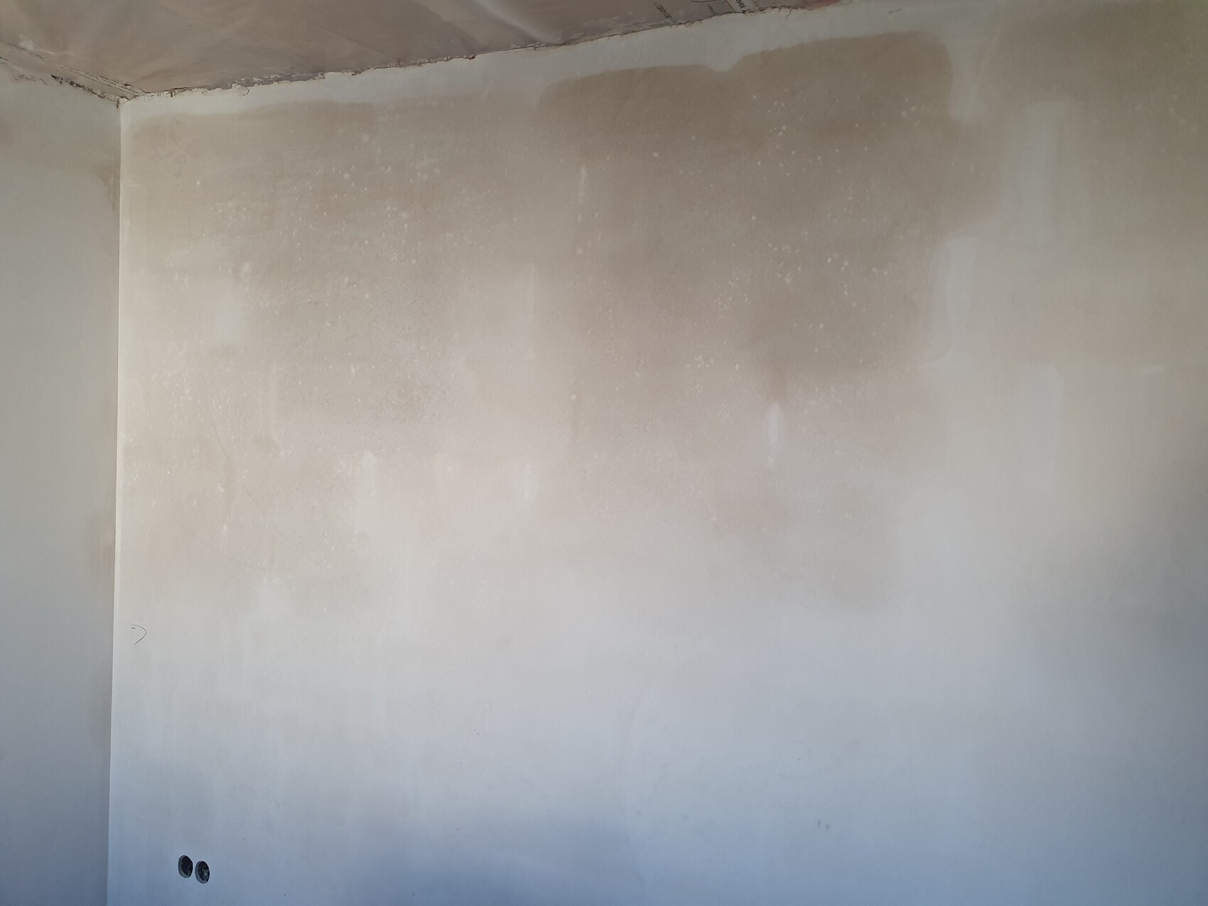 Unverputzte Innenwand mit Putzflecken, Ecke sichtbar, zwei Löcher unten links.