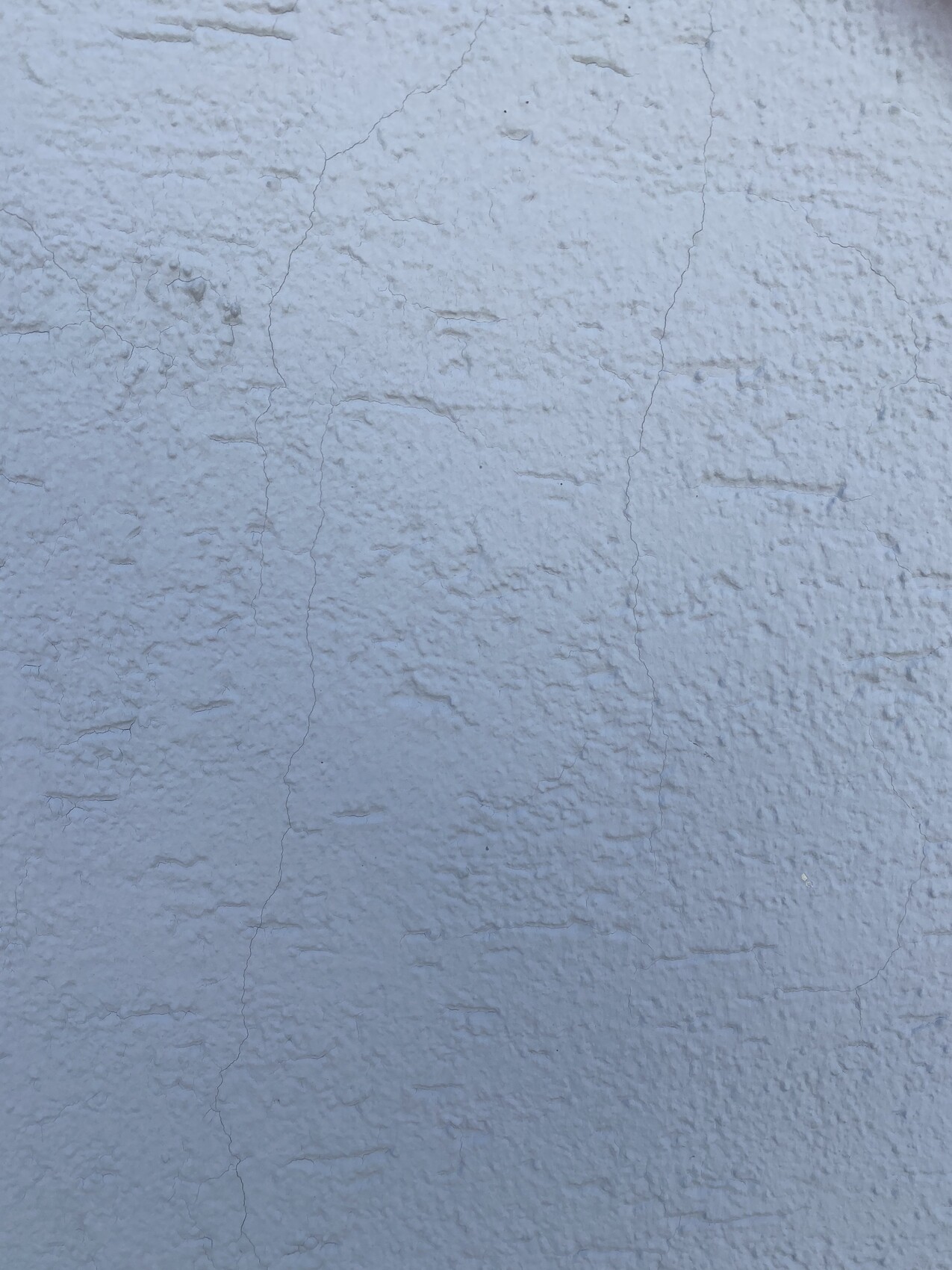 Hellblaue, grob strukturierte Wand mit sichtbaren Rissen und rauer Oberfläche.