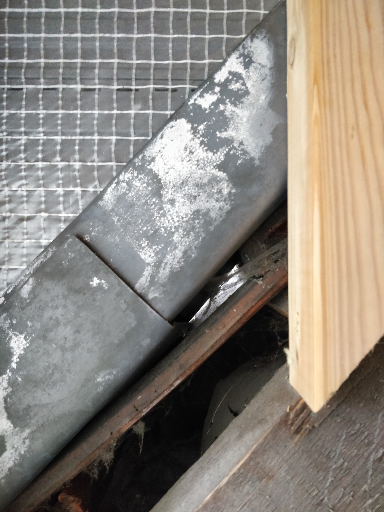 Nahaufnahme eines schrägen Metallrohrs mit Kalkbelag; daneben Holz und Drahtgitter.
