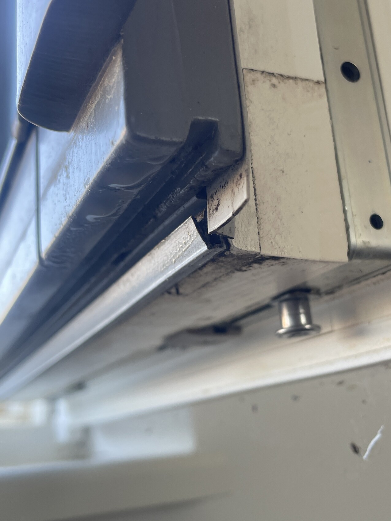 Nahaufnahme eines grauen Metallrahmens mit Nut und Schraubenkopf, leicht verschmutzt.