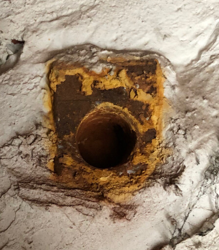 Nahaufnahme einer verrosteten Rohrdurchführung in einer Betonwand mit Kalkablagerungen