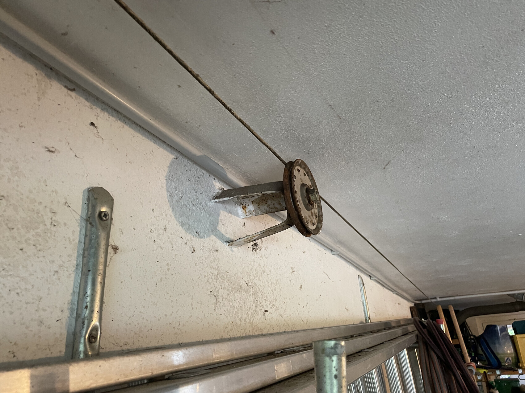 Verrostete Rundrolle mit Halterung an Garagenwand unter der Decke; Seil verläuft darüber.