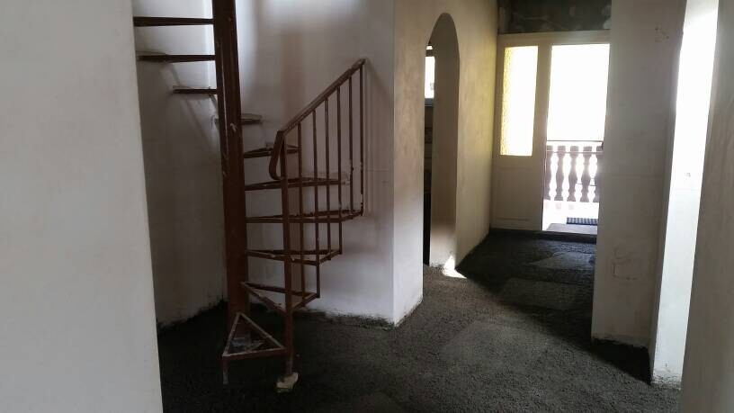 Innenbereich mit verrosteter Spindeltreppe im Flur, offene Tür am Ende