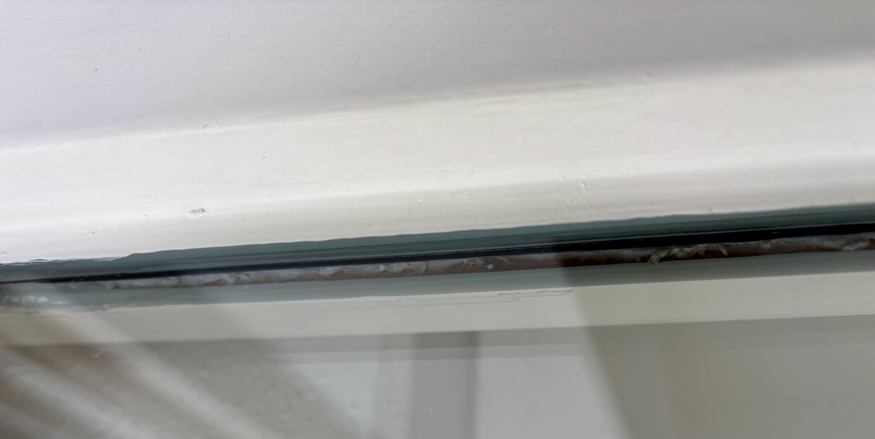 Nahaufnahme eines weißen Fensterrahmens mit Rost im Führungsschlitz und Staub.
