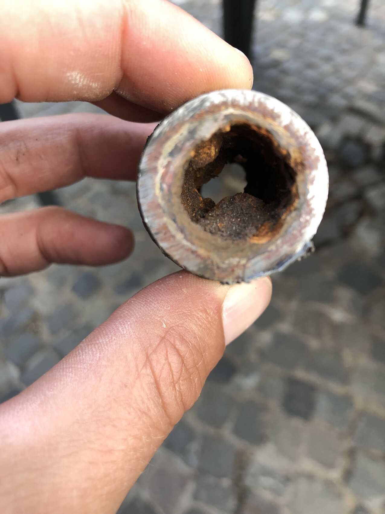 Nahaufnahme eines verrosteten Rohrstücks mit Loch, von Fingern gehalten