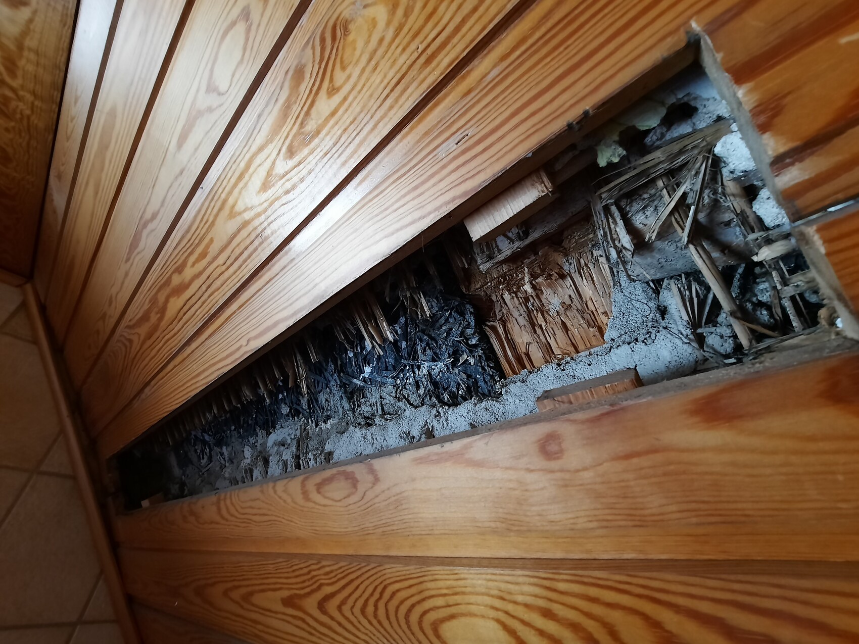 Offene Wandverkleidung mit innerem Hohlraum, verbranntem Holz, Asche und zersplitterten Brettern.