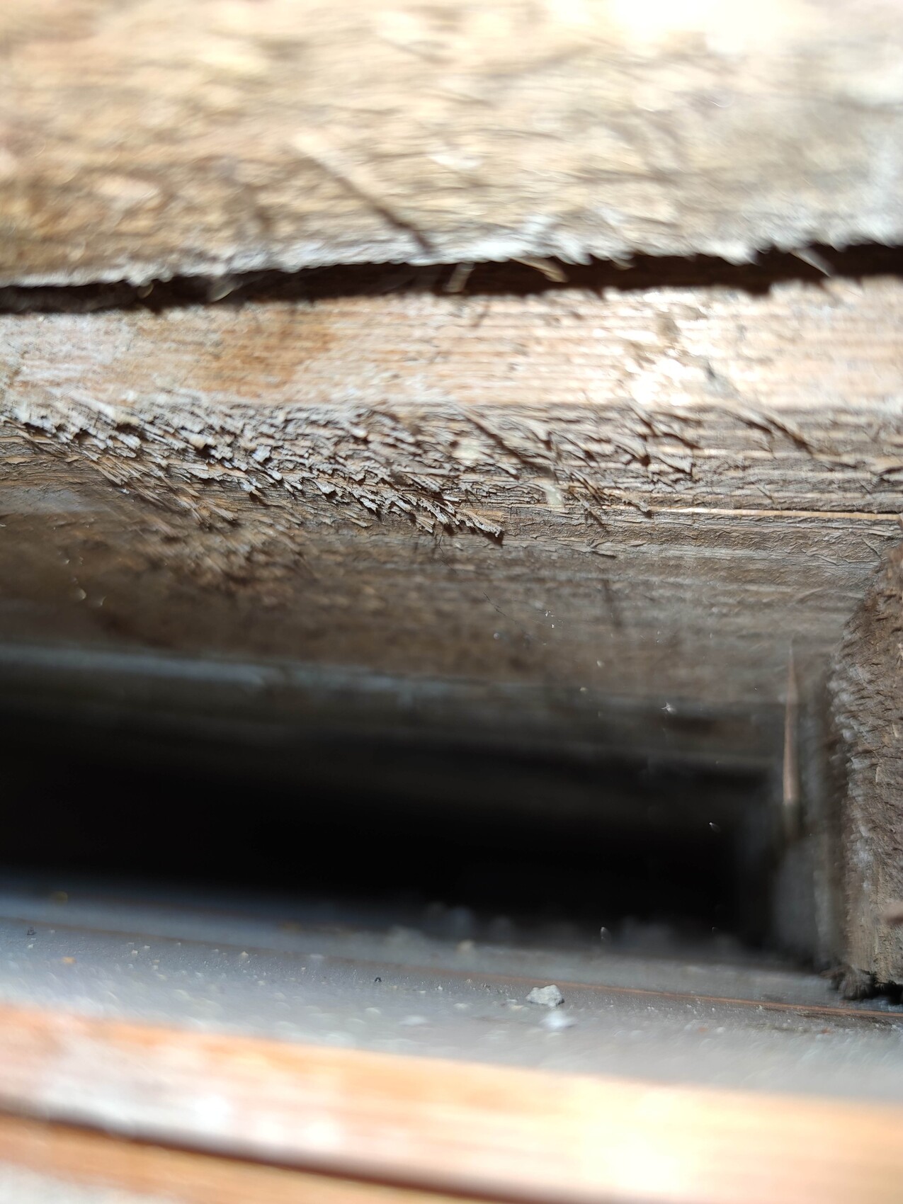 Nahaufnahme von rauem, splitterigem Holz mit dunkler Öffnung darunter