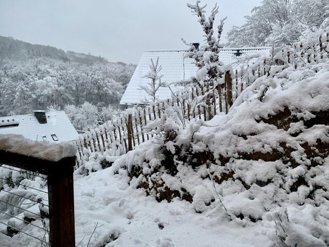 Schneebedeckte Landschaft mit Holzzaun am Hang, Häusern und Bäumen im Winter.