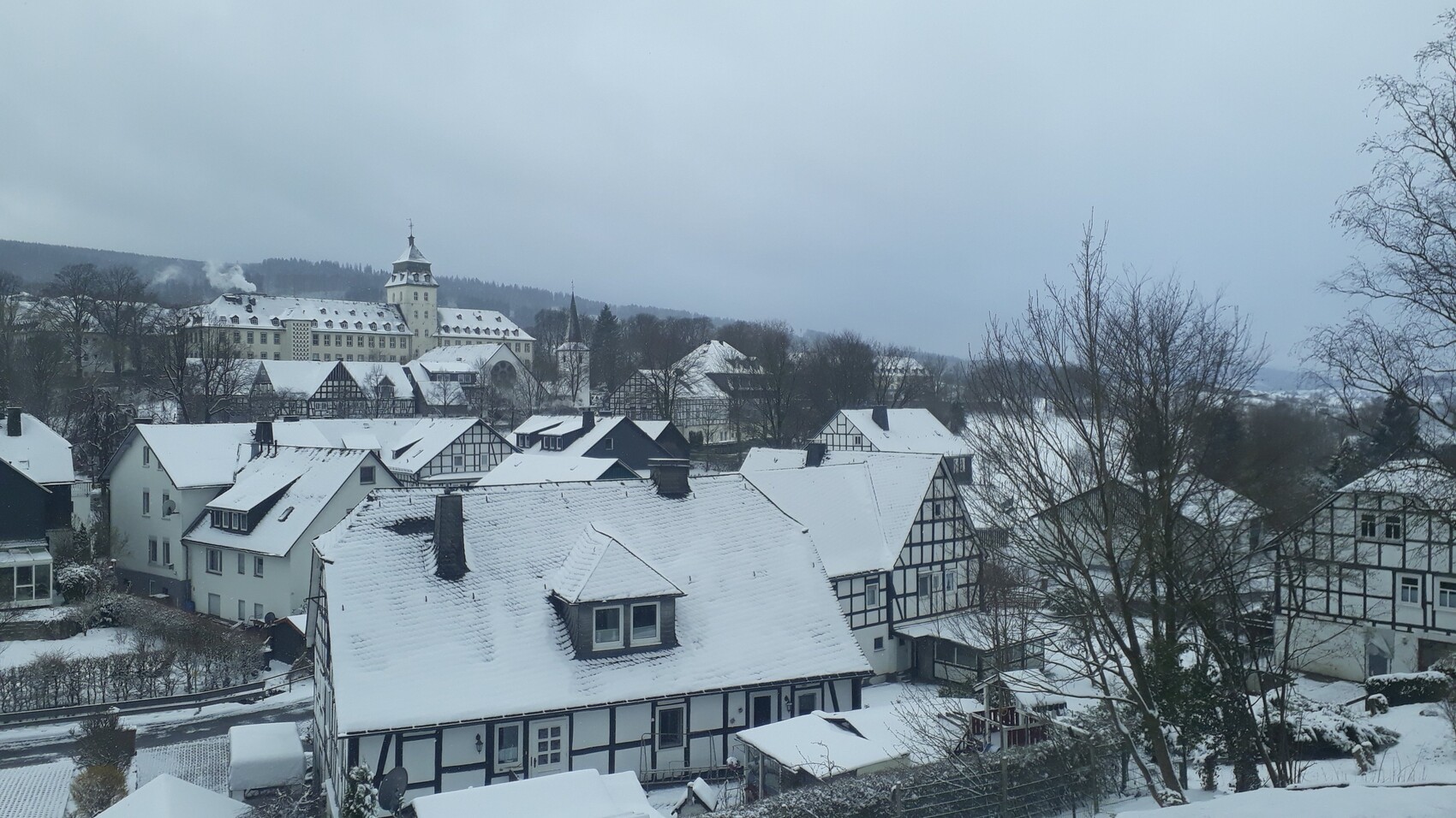 Winterliches Stadtpanorama mit schneebedeckten Fachwerkhäusern, Kirchturm und Schloss.
