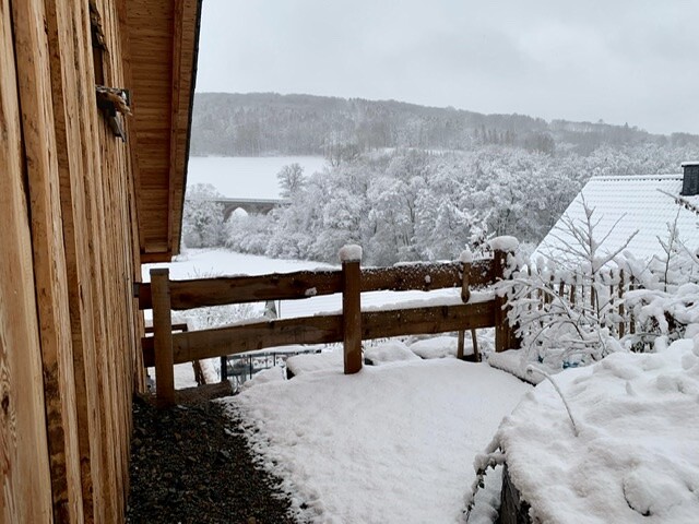 Holzhaus am verschneiten Hof mit Geländer, verschneiter Weg und winterliche Landschaft