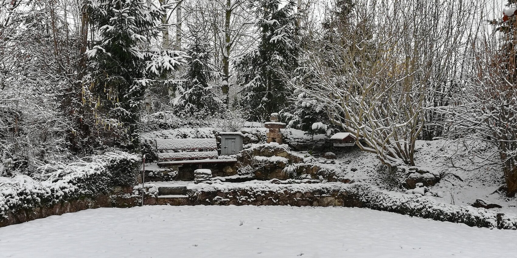 verschneiter-garten-mit-bank-steingarten-und-vogelhaus-im-winter.jpg