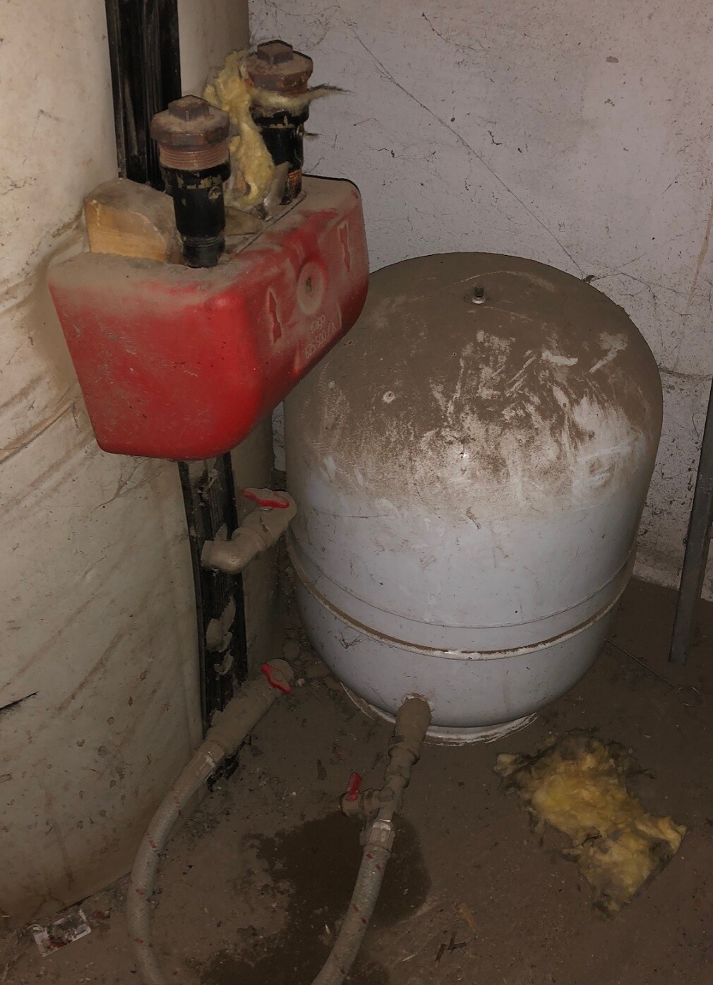Keller: roter Ausdehnungstank neben grauem Drucktank, Rohrleitungen und Staub.