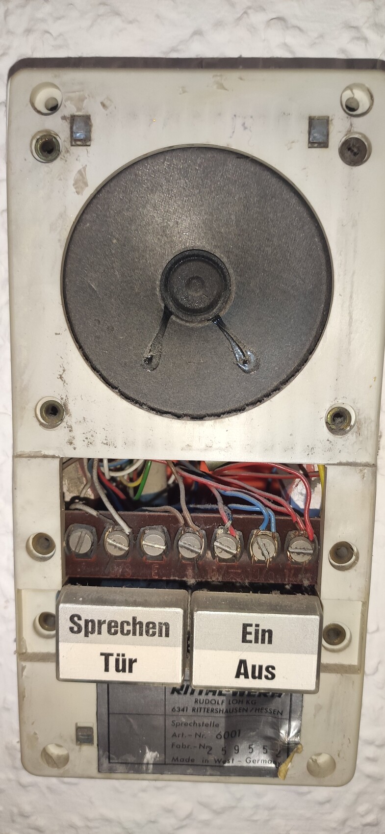Alte Wand-Gegensprechanlage mit Lautsprecher, Kabeln und zwei Tasten: Sprechen/Tür und Ein/Aus.