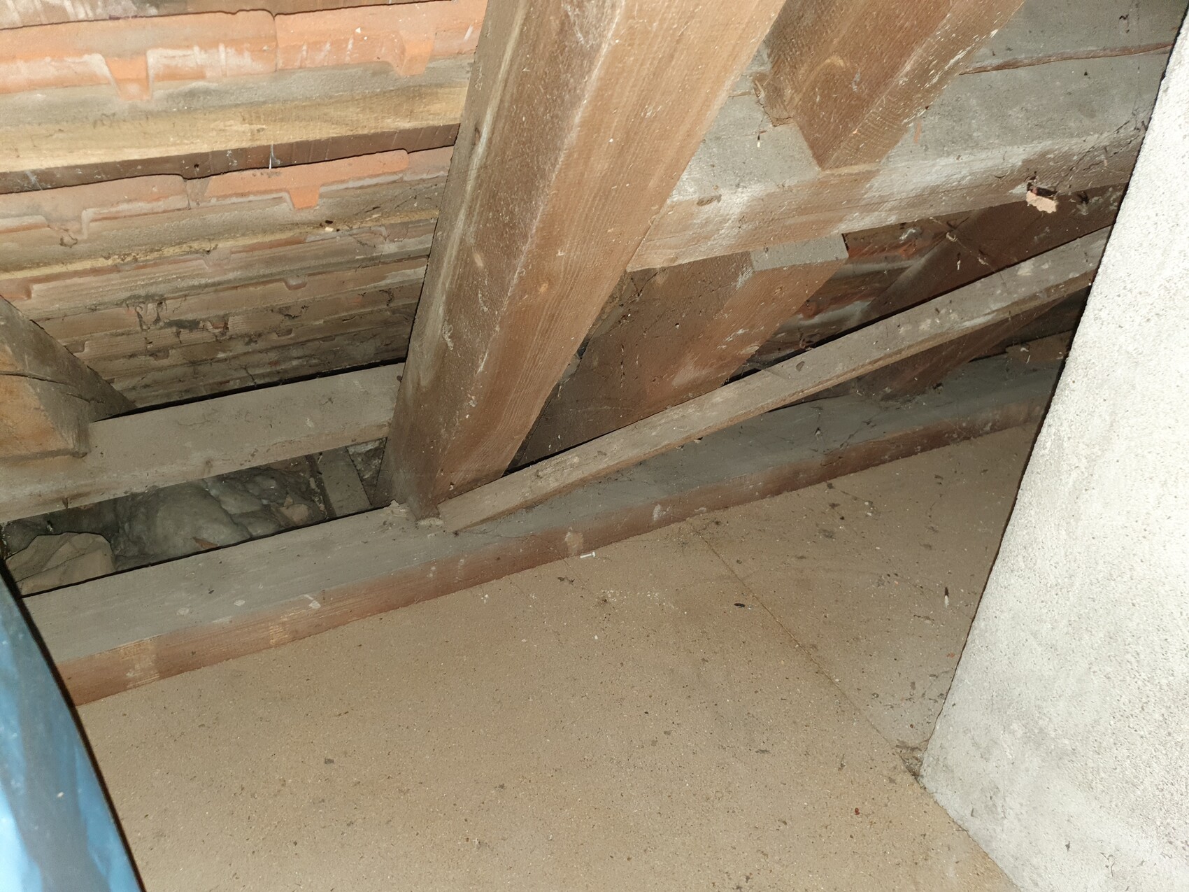 Dachboden mit sichtbaren Holzbalken, Dachlatten, Staub und Spinnweben.