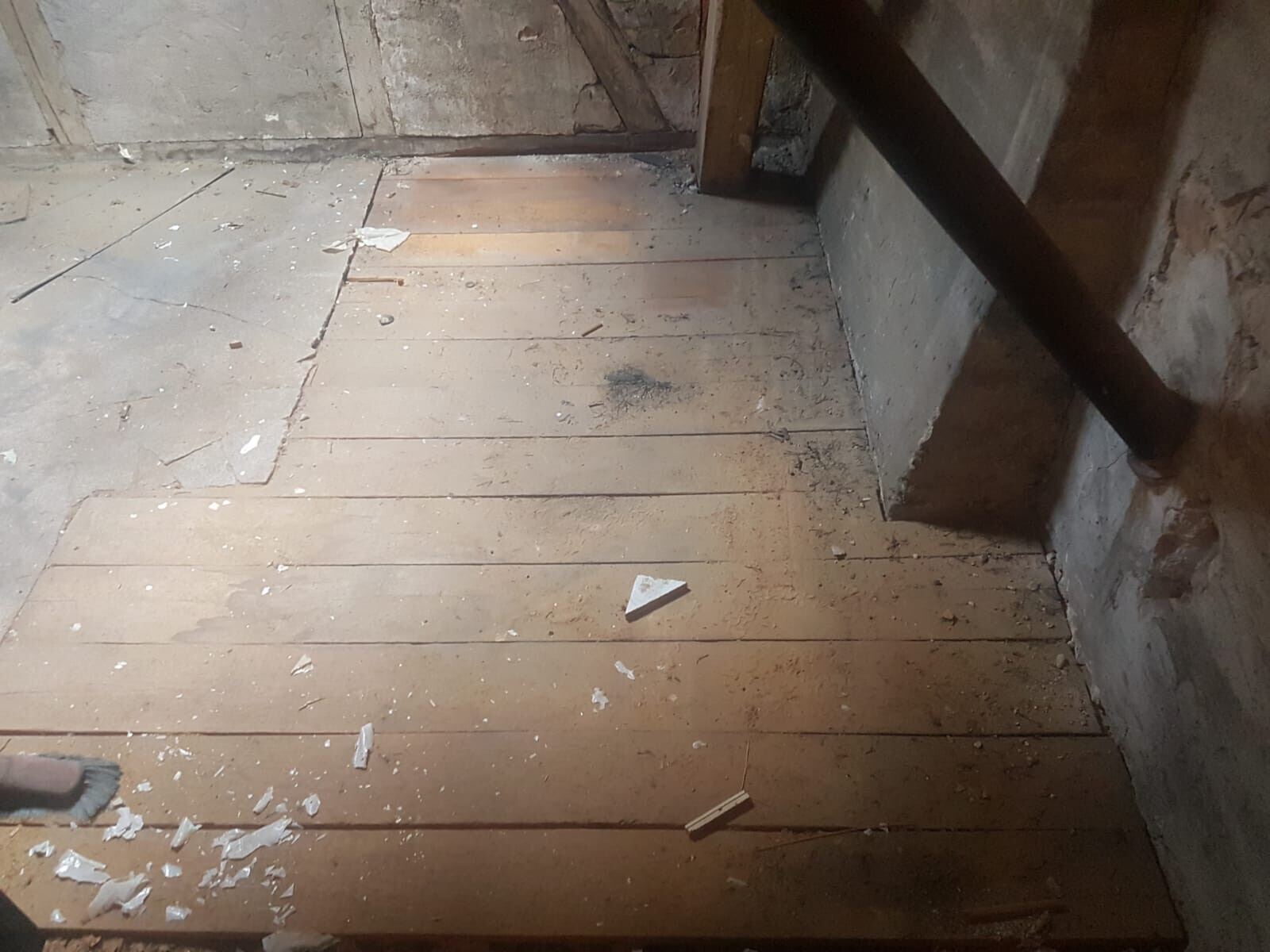 Staubiger Dachboden mit Holzdielenboden, verstreute Trümmer und diagonaler Balken.