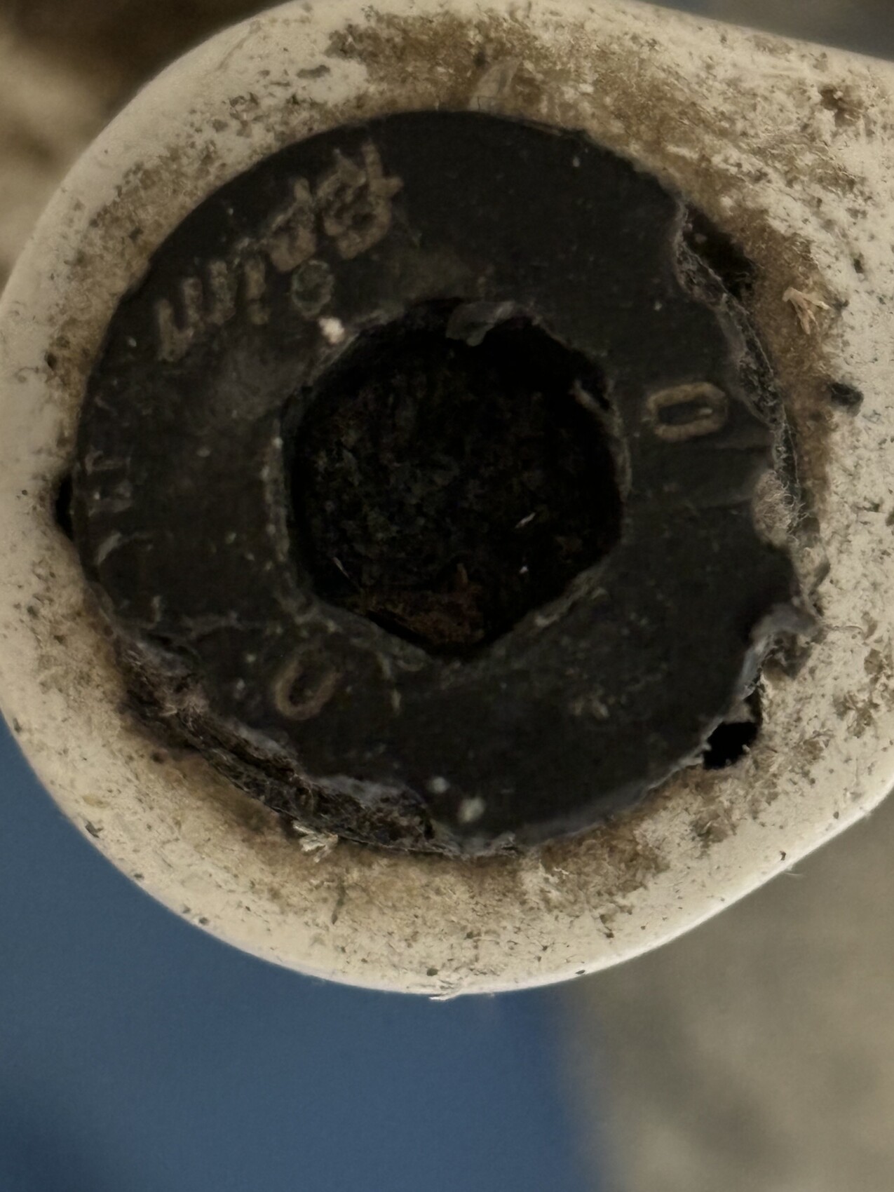 Nahaufnahme eines staubigen Rohrabschlusses mit dunklem Innenloch und umlaufender Beschriftung