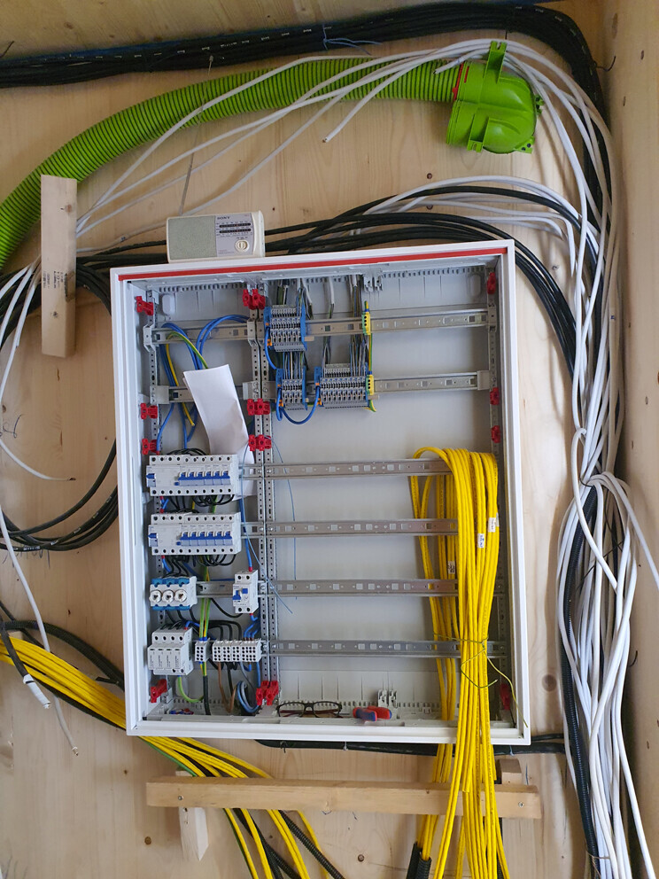 Elektrischer Schaltschrank mit Verteiler, vielen Kabeln und Klemmen an einer Holzwand montiert