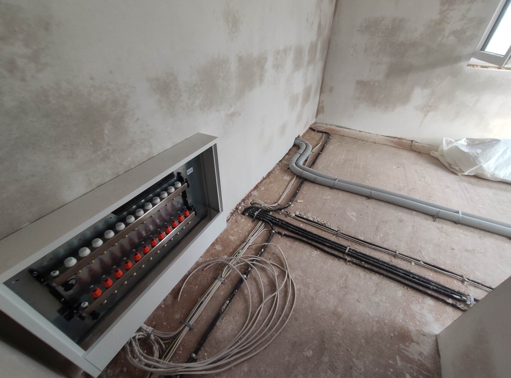Unfertiger Raum mit Verteilerschrank, Kabelbündeln, flexiblen Rohren und Betonboden.