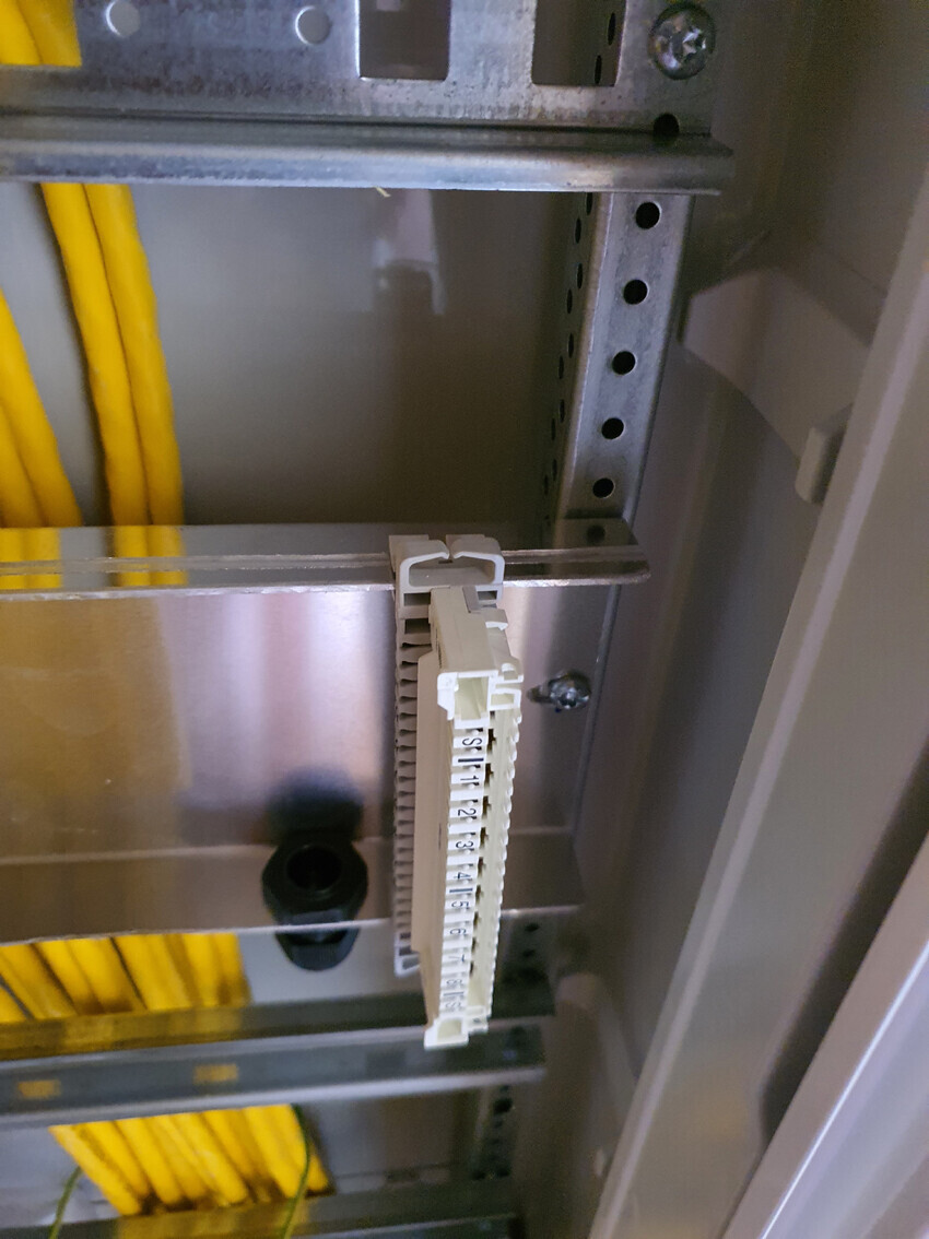 Schaltschrank: Weißer Terminalblock an DIN-Schiene, gelbe Kabel links daneben.