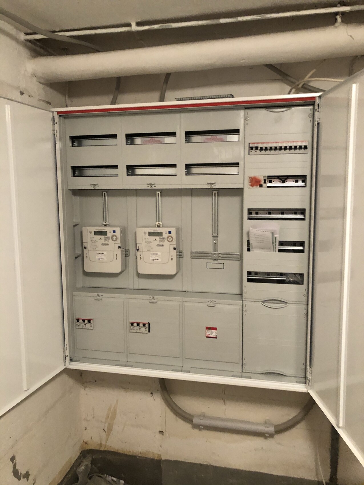Großer elektrischer Verteilerschrank mit zwei Stromzählern, Schienen und Sicherungen.