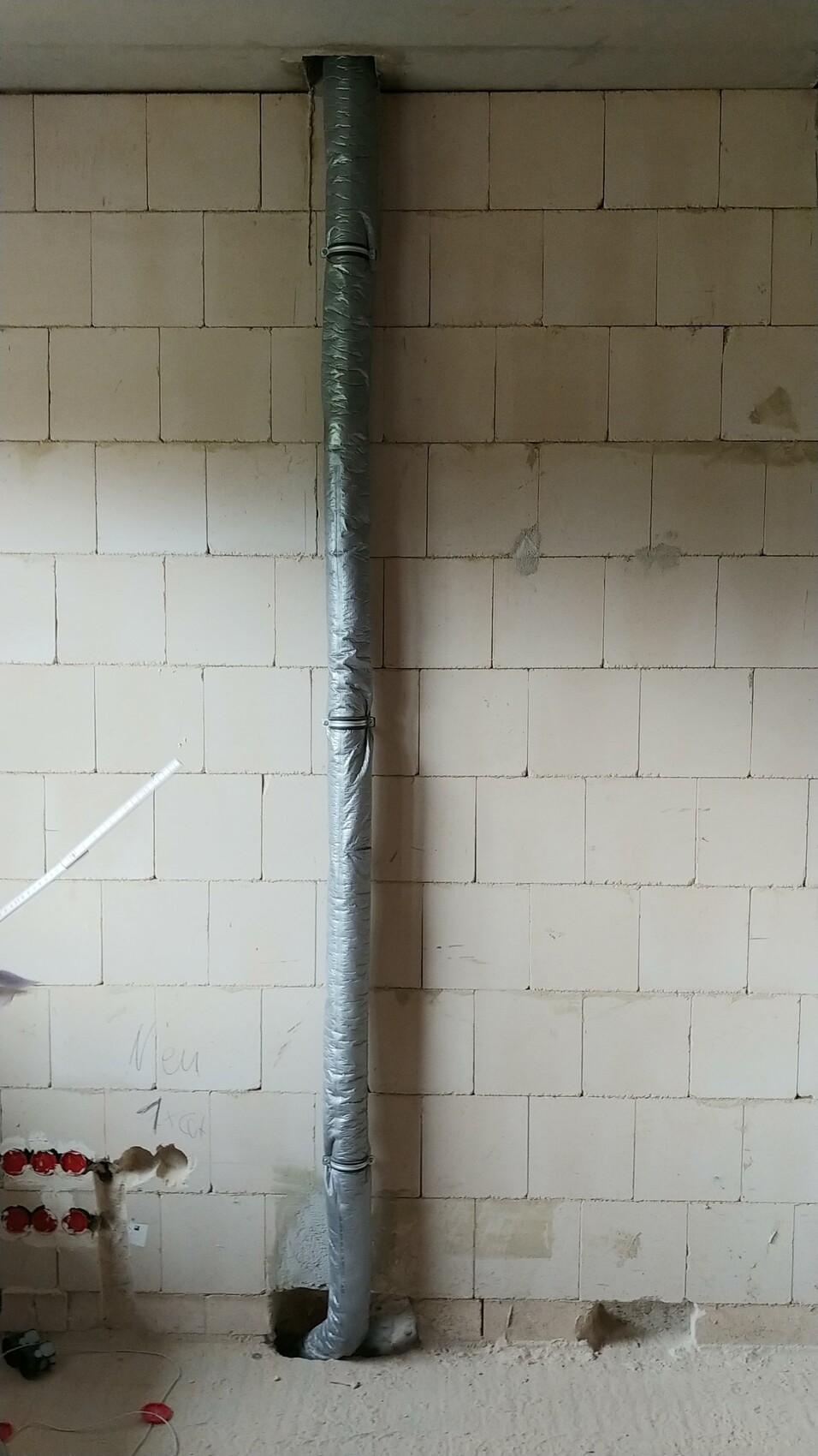 Vertikales isoliertes Installationsrohr steht an einer verputzten Wand in einem Bauprojekt.