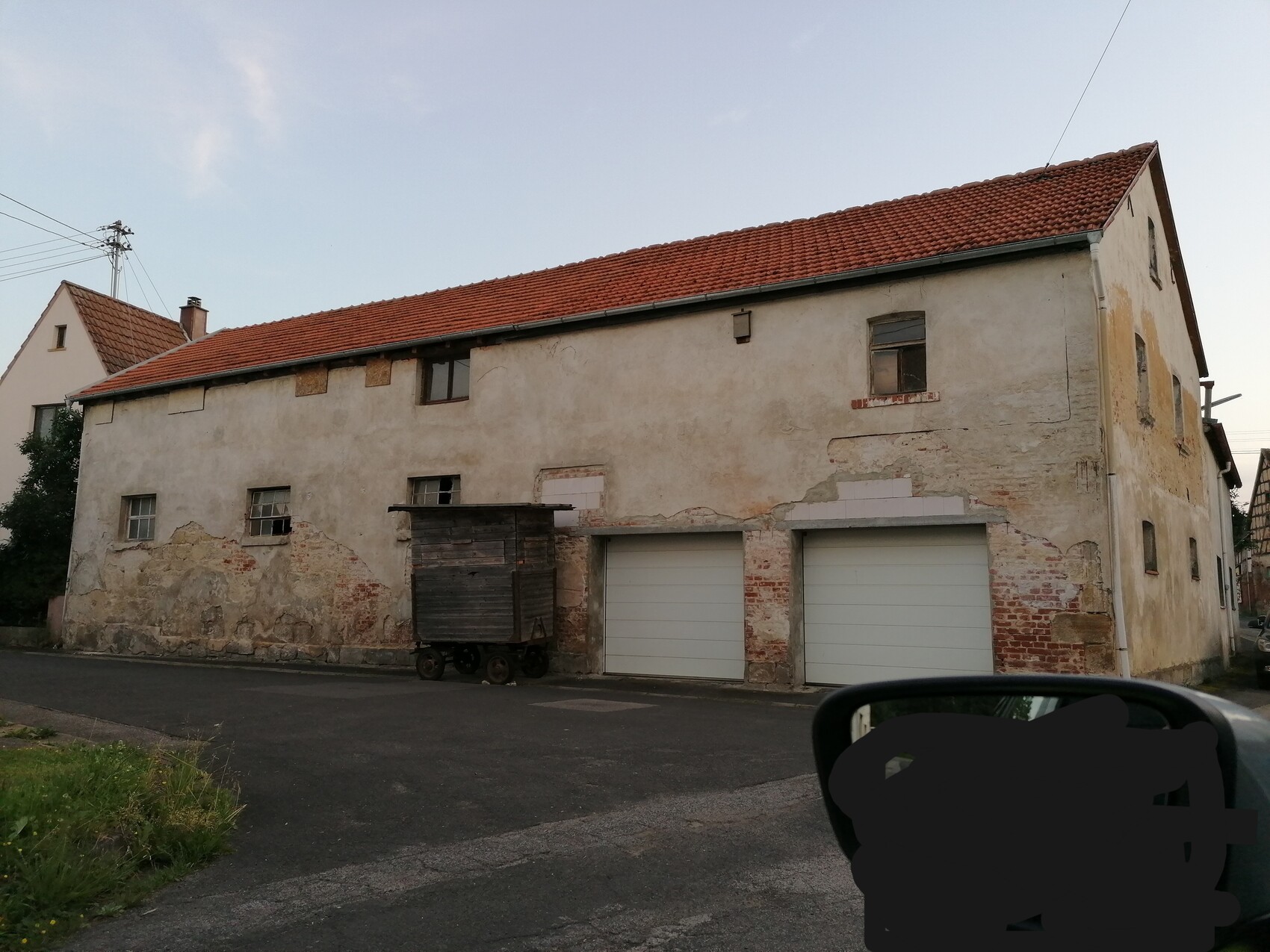 Altes Gebäude mit abblätternder Verputzfassade, zwei Garagen-Tore und rotem Dachziegeln.