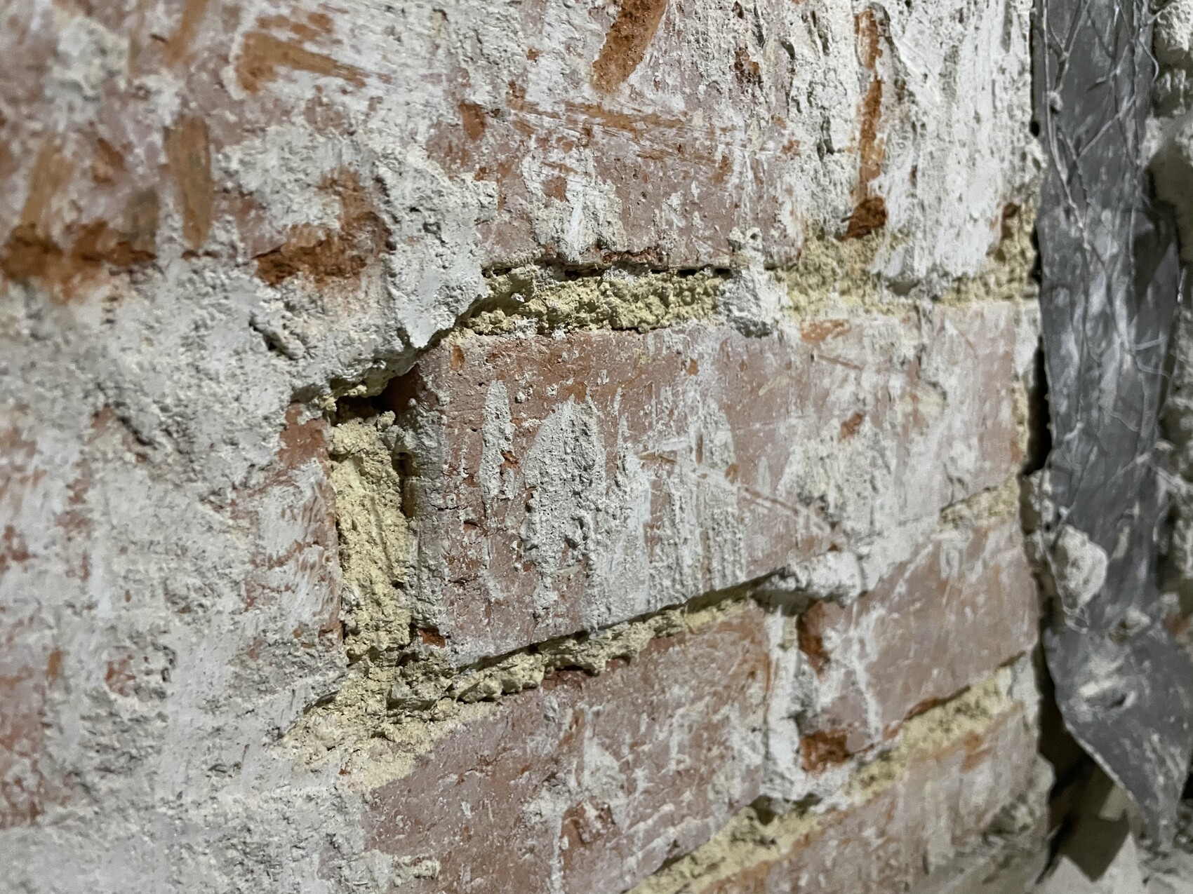 Nahaufnahme einer alten Ziegelwand mit bröckelndem Mörtel und Staub