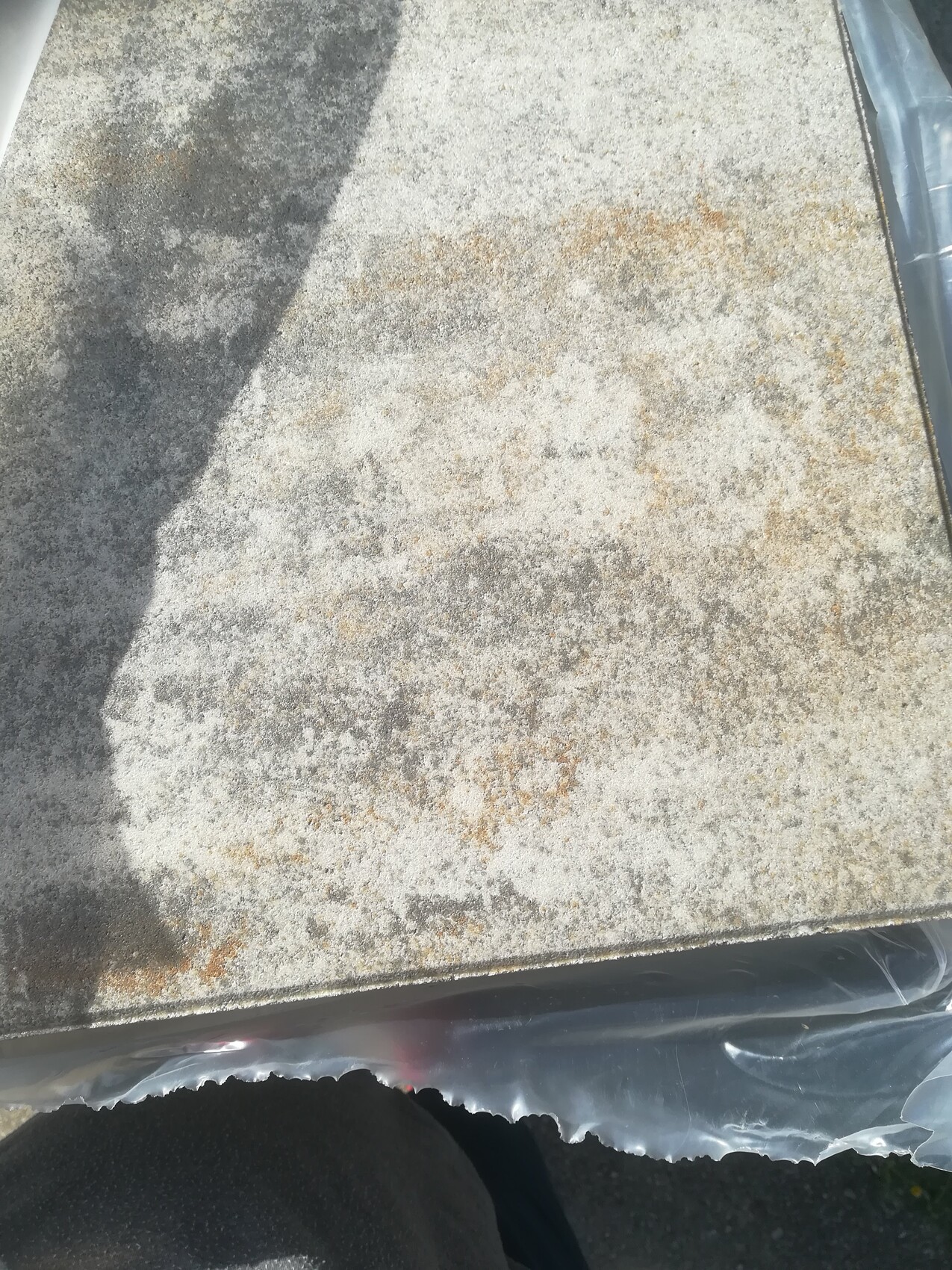 Nahaufnahme einer grauen Stein-/Betonplatte mit weißer Salzeffloreszenz und Schatten.