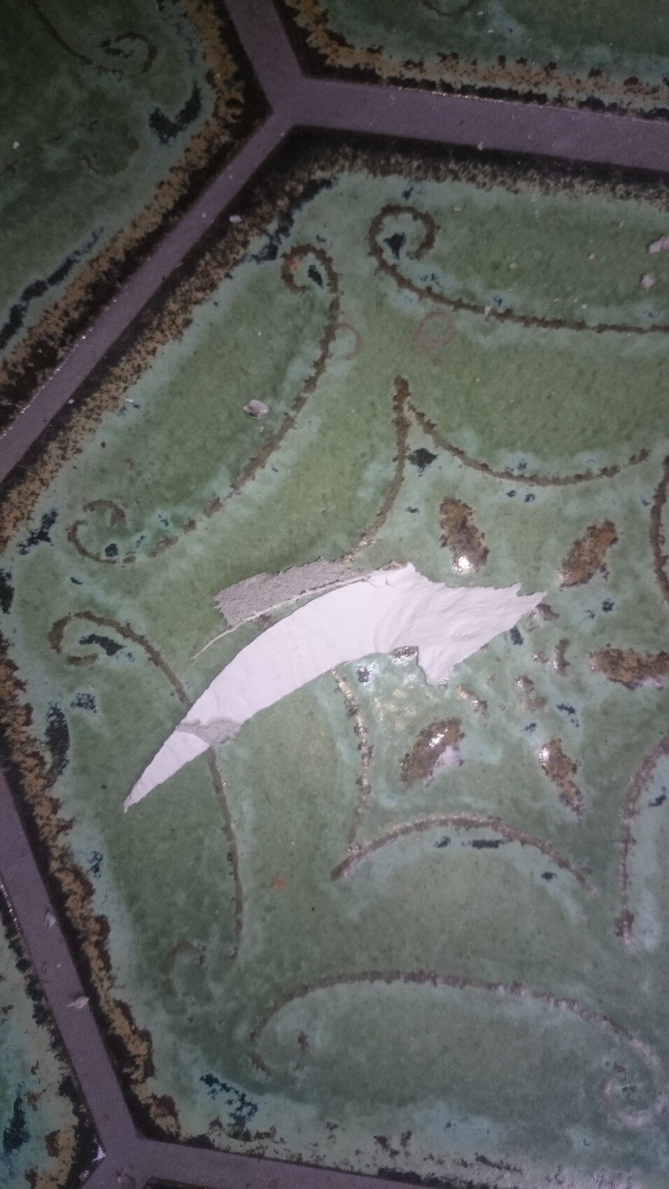 Grüne Fliese mit braunem Spiralmuster; eine abgebrochene weiße Scherbe liegt darauf