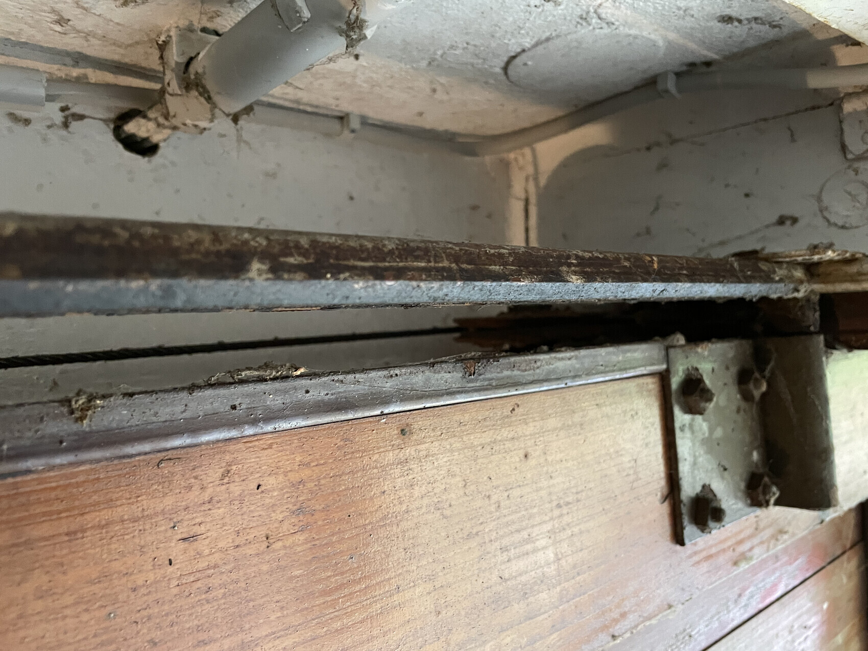 Verrostete Metall-Schiene liegt auf altem Holzboden, Staub und Dreck verstreut.