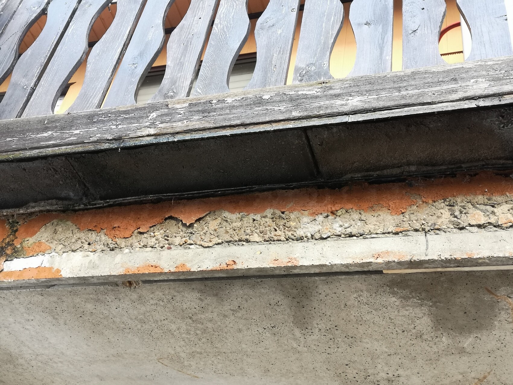 Altes Balkongeländer aus Holz mit ovalen Ausschnitten über bröckelnder Putzwand.