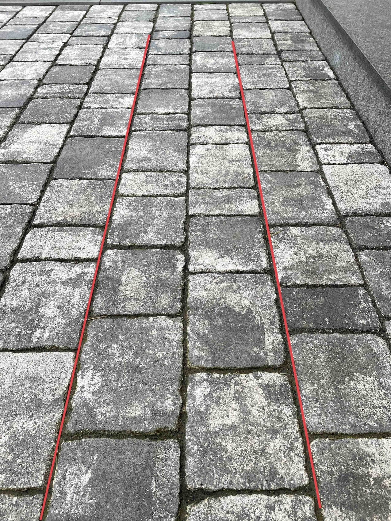 Gepflasterter Steinweg mit zwei roten Linien, die einen Pfad markieren.