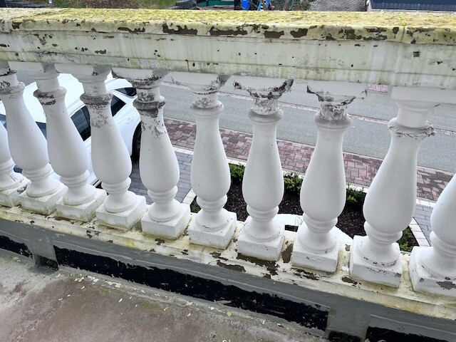 Weiße Balustrade mit abblätternder Farbe und moosiger Oberkante, Blick auf die Straße.