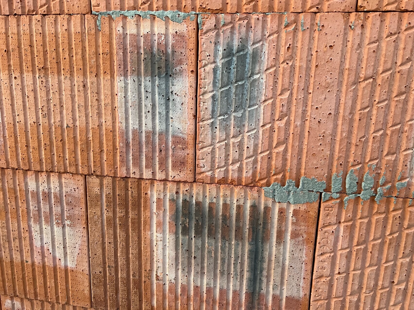 Nahaufnahme roter Klinkersteine mit vertikalen Rillen und blau-grauer Farbschmiererei.