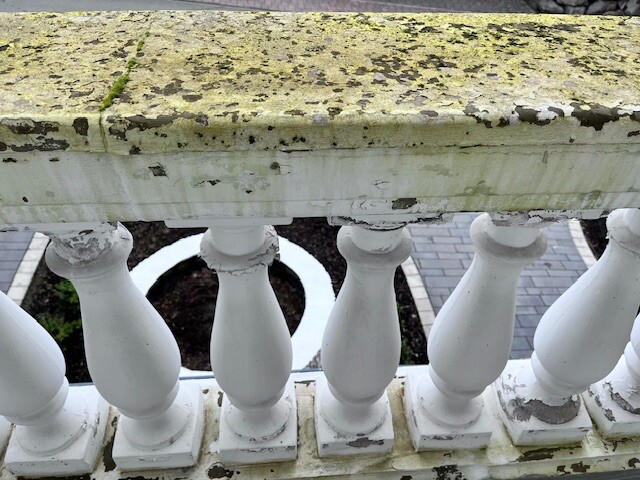 Weißes Balustraden-Geländer mit abgeplatzter Farbe und Moos auf der Steinplatte.