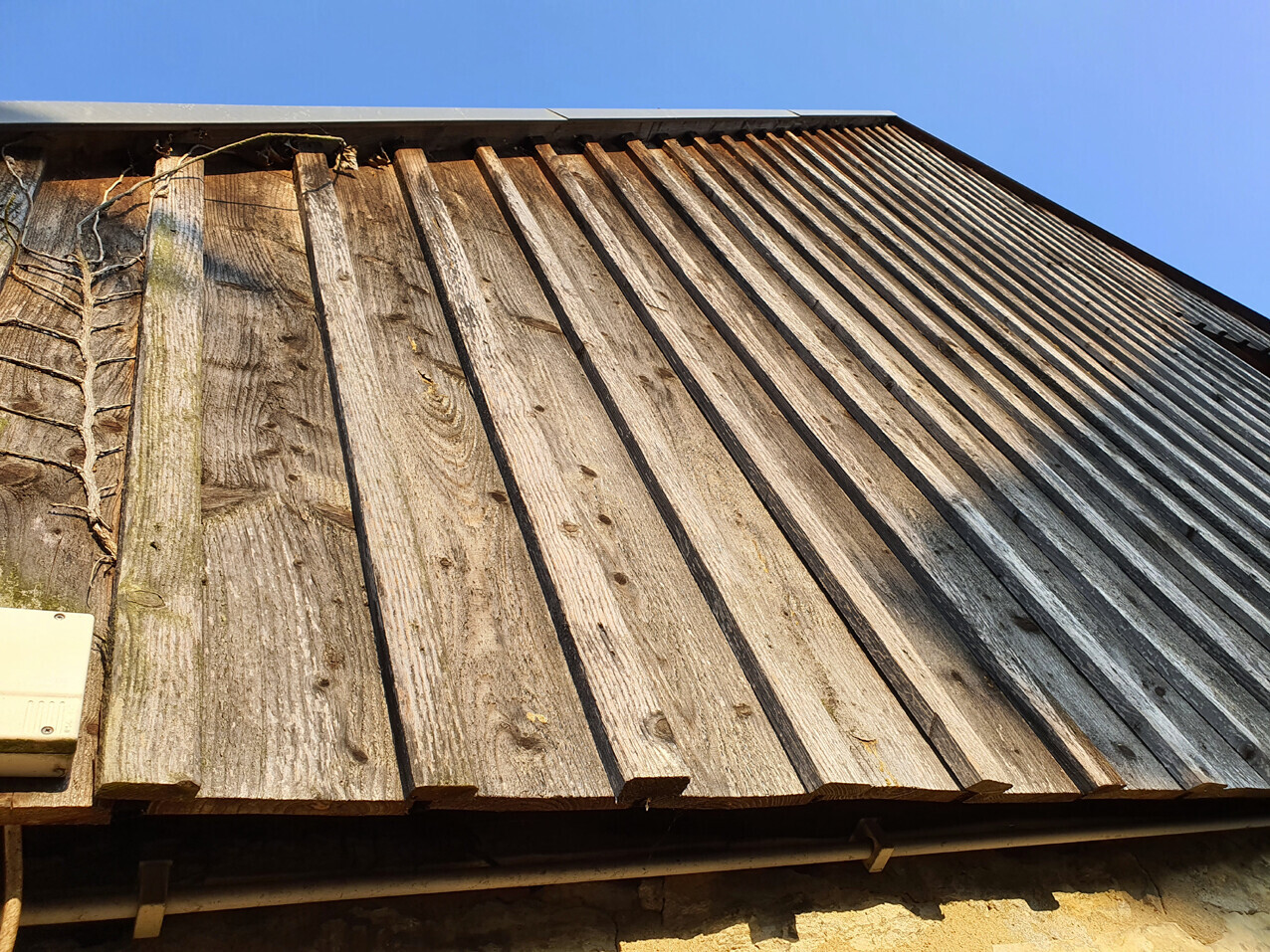Verwittertes Holzdach aus langen Brettern, Blick von unten, blauer Himmel.