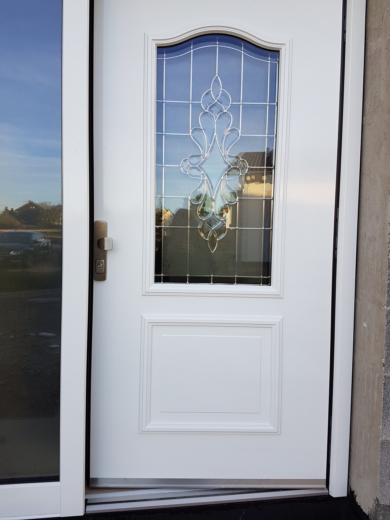 Weiße Haustür mit dekorativem Glasfenster in der Mitte, Griff links.