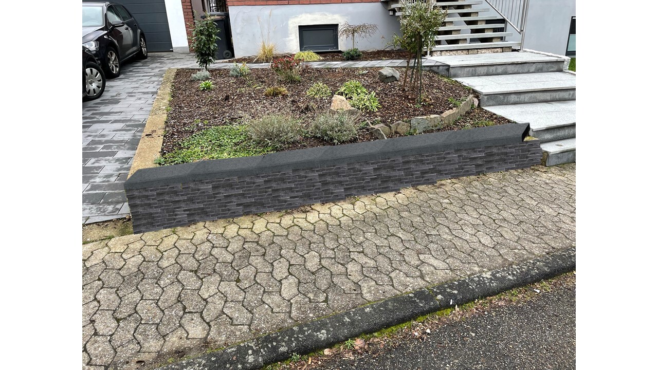 Vorgarten mit dunkler Steinmauer, Pflanzbeet und Treppenaufgang zur Haustür.