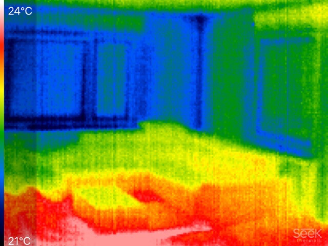 Thermografisches Bild eines Zimmers: warmer Boden, kühlere Wände; ca. 21–24 °C.