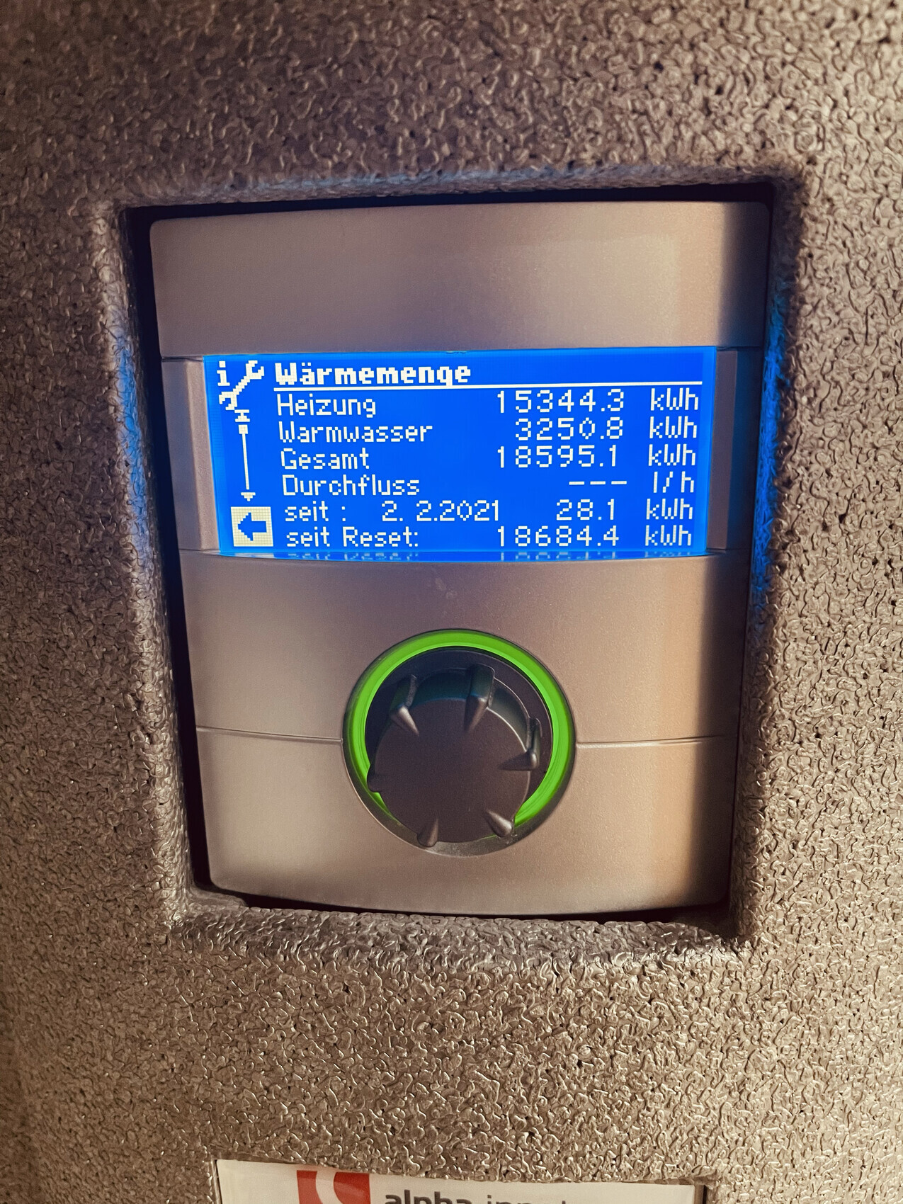 Blaue Displayanzeige einer Heizungsanlage mit grünem Rundknopf; Werte: Heizung, Warmwasser.