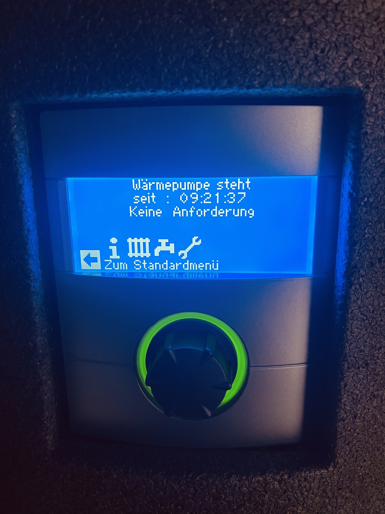 Blaues Display einer Heizungssteuerung mit Text: Wärmepumpe steht seit 09:21:37, Grüner Ringknopf.
