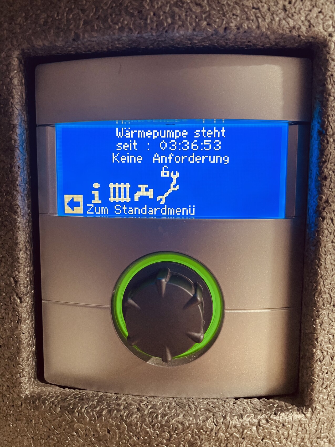 Blaues Display eines Wärmepumpen-Steuergeräts mit grünem Drehknopf und Statusanzeige.
