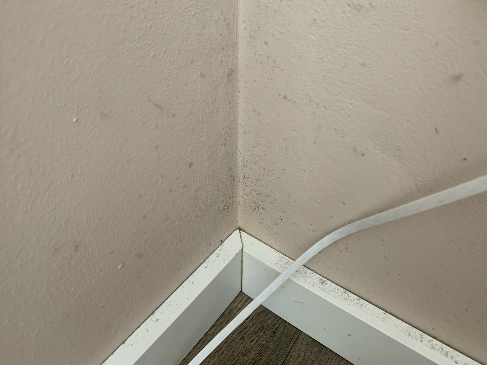Wand-Ecke mit Flecken am Sockelbereich und sichtbares Kabel.