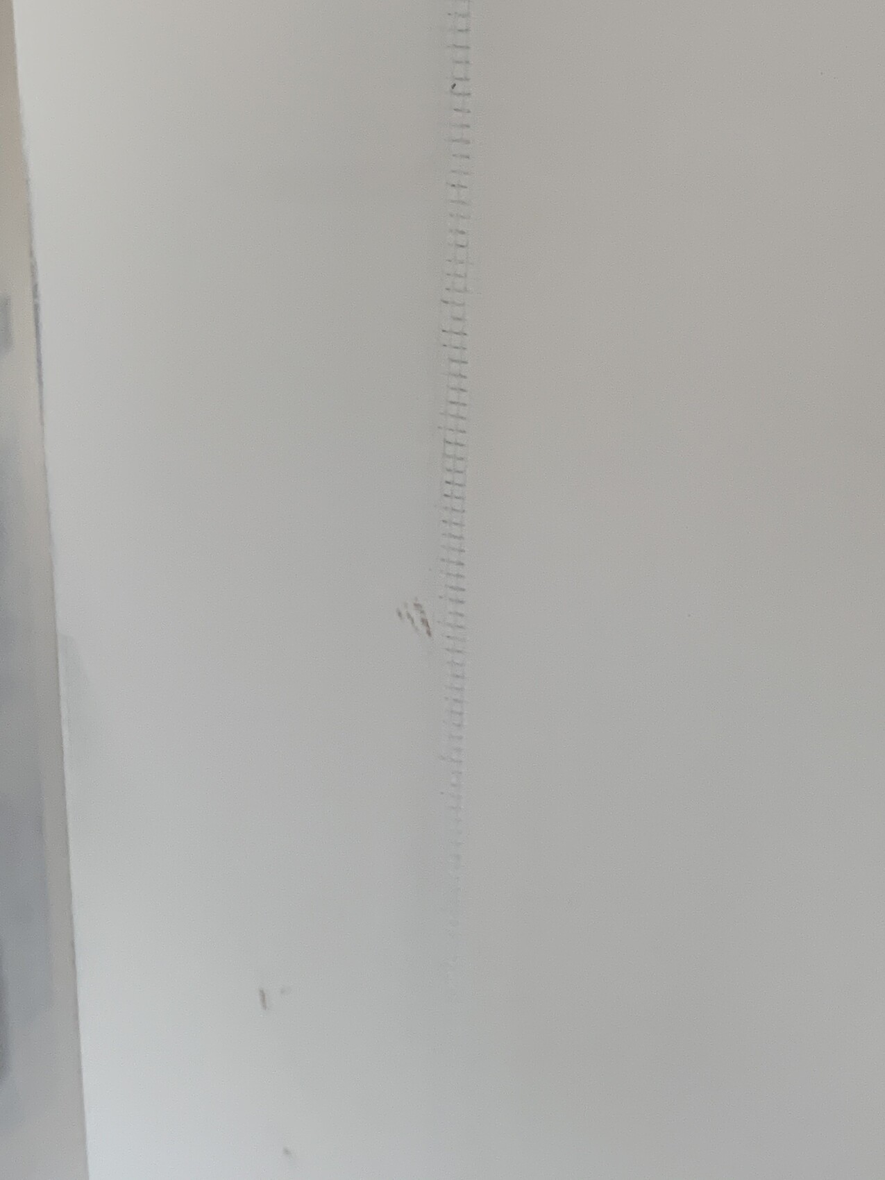 Senkrechte Messlatte mit feinen Markierungen an weißer Wand.