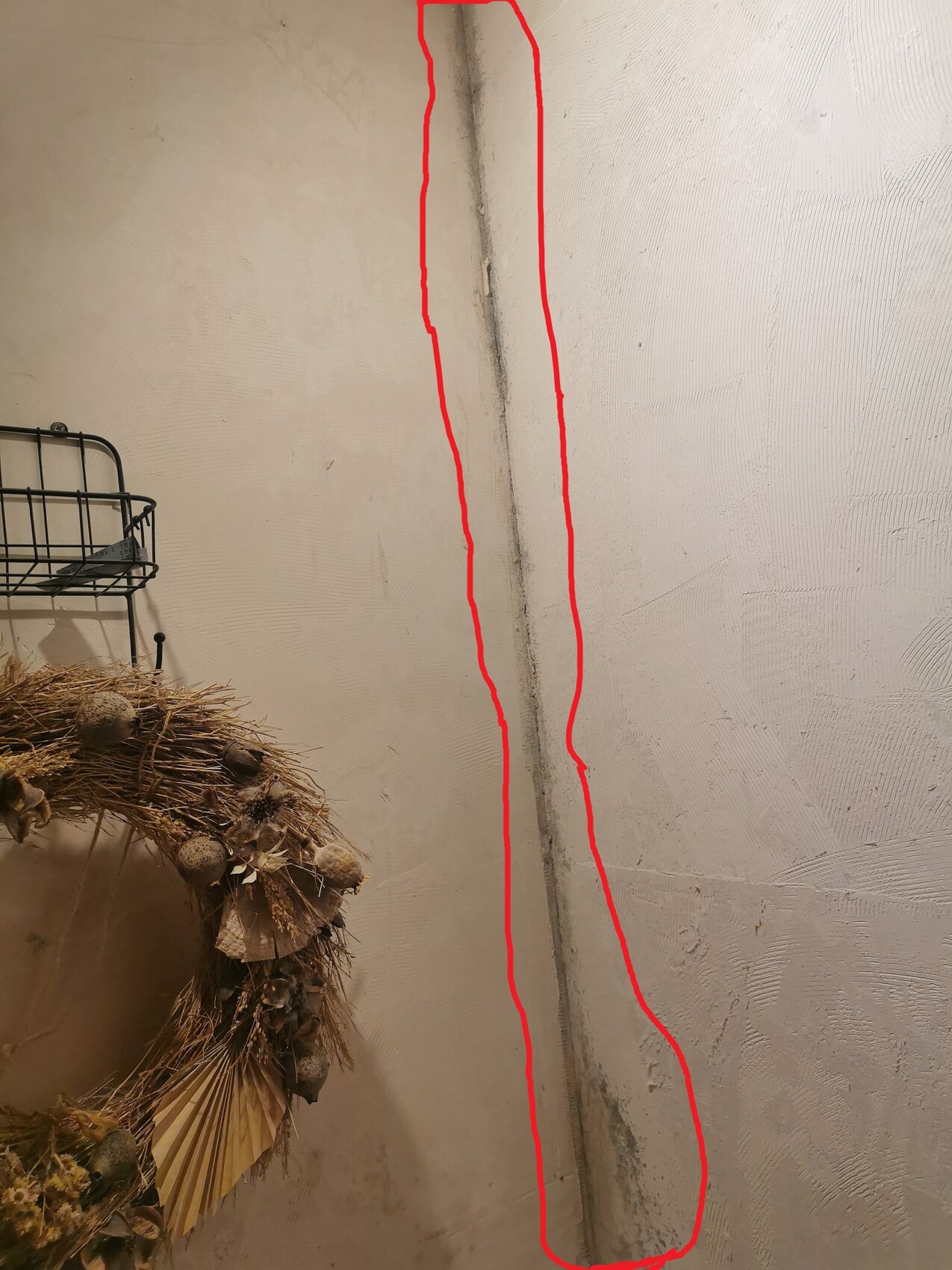 Senkrechter Riss entlang der Ecke einer verputzten Wand; links unten hängt ein Trockenkranz.