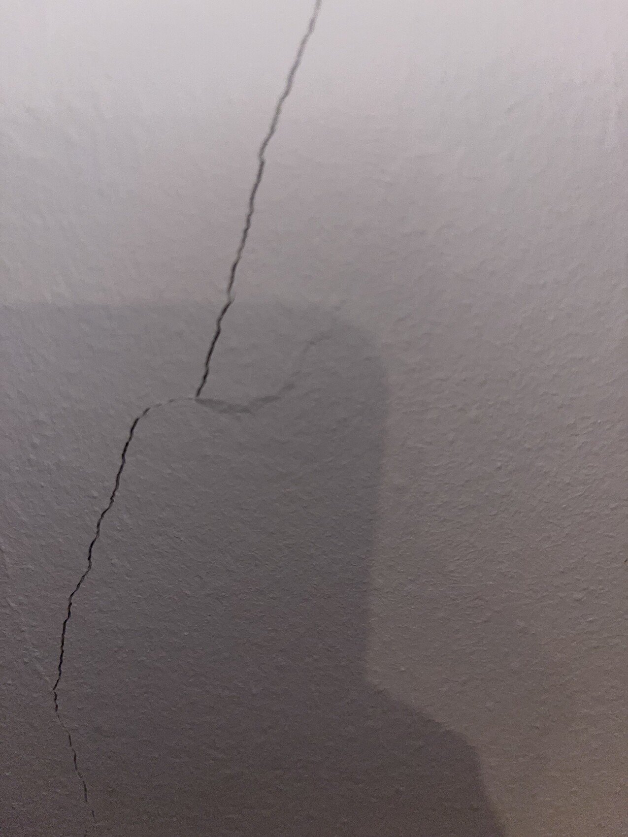 Weiße Wand mit einem langen, unregelmäßigen Riss und Schatten.